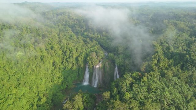 Aerial view of Cikaso Waterfall cascading into a turquoise pool surrounded by lush tropical forest and morning mist in Sukabumi, West Java, Indonesia.