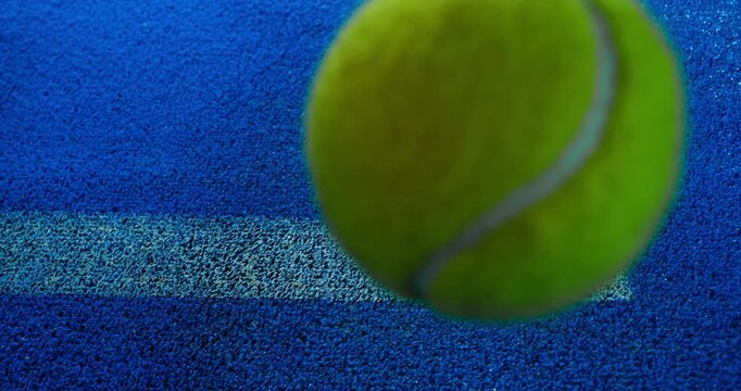 Extreme super slow motion close-up of a tennis or padel ball bouncing near the court line. Detailed blue surface texture captured at 1000fps with dynamic sports action in macro detail.