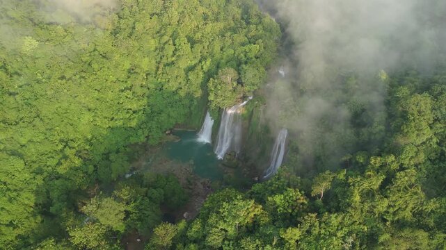 Aerial view of Cikaso Waterfall with its three falls and turquoise pool surrounded by dense tropical forest and morning mist Sukabumi, West Java, Indonesia.
