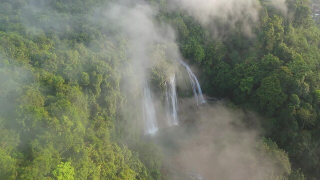 Aerial view of Cikaso Waterfall partially obscured by thick mist and clouds surrounded by lush tropical forest in Sukabumi, West Java, Indonesia.