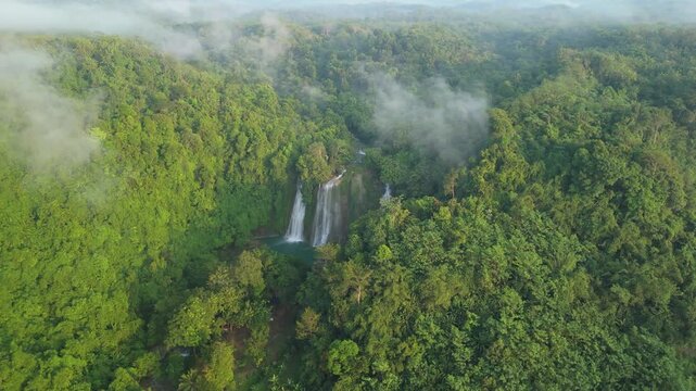 Aerial view of Cikaso Waterfall surrounded by dense tropical jungle and morning mist over the lush green canopy Sukabumi, West Java, Indonesia.