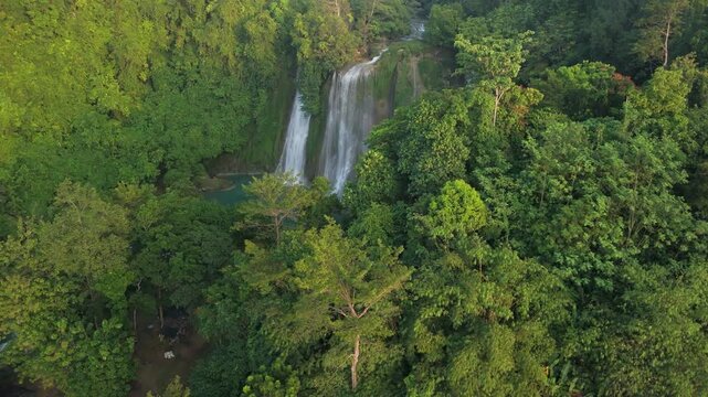 Aerial view of Cikaso Waterfall cascading into a turquoise pool surrounded by dense tropical jungle and lush green trees in Sukabumi, West Java, Indonesia.