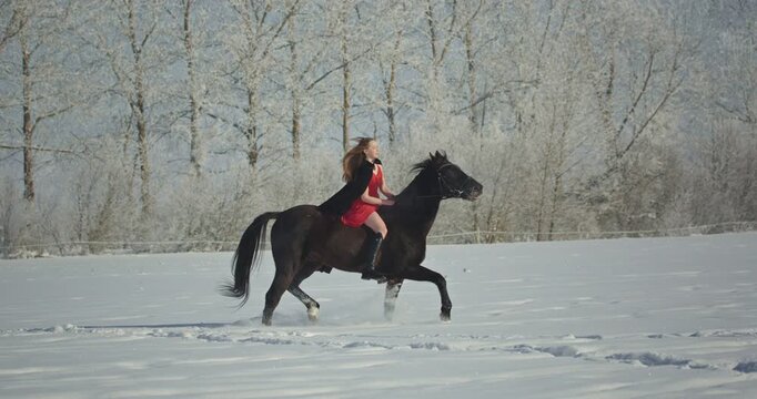 Beautiful woman in red dress riding horse in winter