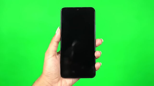Close-up shot of a hand holding a modern black smartphone with a blank screen against a vibrant green chroma key background, ideal for digital content insertion and app demonstrations