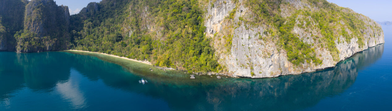 Calm water bathes a dramatic limestone island in Bacuit Bay, El Nido. This scenic area in the Philippines is a popular vacation destination due to its coral reefs, beaches, and hidden lagoons.