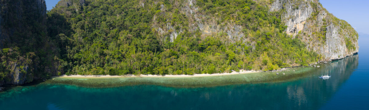Calm water bathes a dramatic limestone island in Bacuit Bay, El Nido. This scenic area in the Philippines is a popular vacation destination due to its coral reefs, beaches, and hidden lagoons.