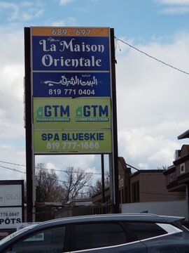 Gatineau, Quebec, Canada &ndash; May 1, 2026: A multi-tenant commercial plaza sign features advertisements for "March&eacute; La Maison Orientale, GTM Construction, and Spa Blueskie" against a cloudy sky on Boul. 