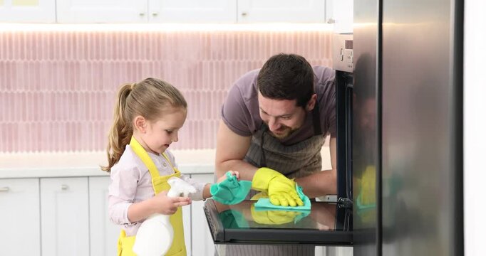 Spring cleaning. Smiling father and daughter wiping oven with rags and bottle of detergent in kitchen