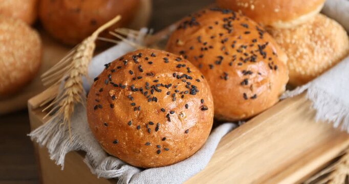 Woman putting wheat ear into wooden box with sesame seed buns at table, closeup