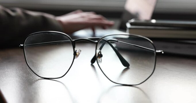 Businesswoman typing on laptop at table, focus on stylish glasses