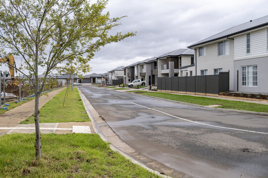 A residential street lined with newly built double-story houses and townhouses in the growth suburb of Tarneit, Victoria, Australia, with a construction site nearby