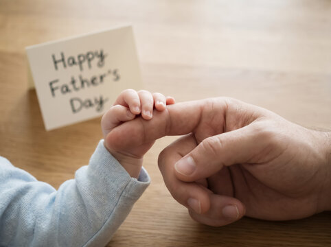 Father holding small baby hand near Happy Fathers Day card