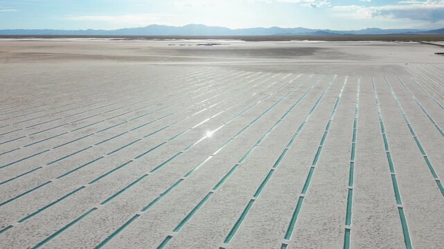 Aerial view of Salinas Grandes salt flats with turquoise rectangular pools and distant mountains under a bright sun in Tumbaya, Jujuy, Argentina.