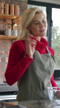 Vertical video: Greeting camera cook in red top, apron in kitchen, using bowl and cutter for baking