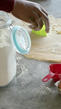 Vertical video: Adult hand entering, stamping cutter into dough on home kitchen counter, for baking