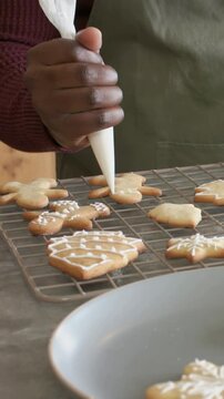 Vertical video: Positioning tip, hand icing cookies on rack at counter with piping bag, olive apron