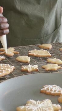 Vertical video: Picking up piping bag, green-apron baker icing cookies at home counter, rack