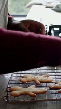 Vertical video: Decorating as hand entering, maroon sleeve hands in apron icing gingerbread on rack