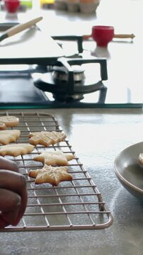 Vertical video: Hand entering maroon sleeve picking star cookies from rack at home placing on plate