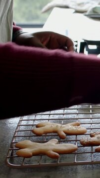 Vertical video: Seeing cooling rack, baker in kitchen in apron adding sprinkles finishing cookies