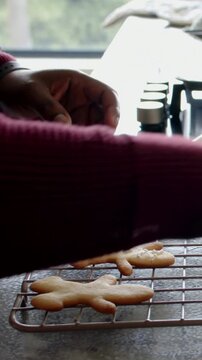 Vertical video: Seeing cooled cookies, baker adding white dots on rack at counter, maroon sweater