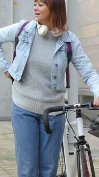 Vertical video: Adjusting denim jacket woman steadying bike checking phone and calling at sidewalk
