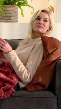 Vertical video: Tapping phone after message, woman in cream sweater scrolling then speaking on sofa