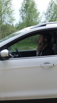 Vertical video man driving a white car, distracted by a smartphone call, ignoring road safety and creating a hazardous situation for himself and others on the road