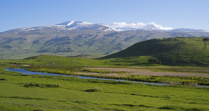 A wide view over a green valley with snow-capped mountains under a clear sky, landscape near Rya Taza with a view of the Aragaz, Ria Taza, Aragatsotn Province, Armenia