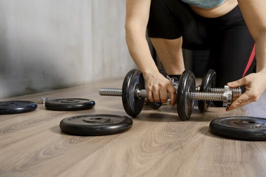 A person is adjusting weights on a dumbbell while preparing for an intense workout. The setting is a well-lit fitness center, with various weights scattered on the floor