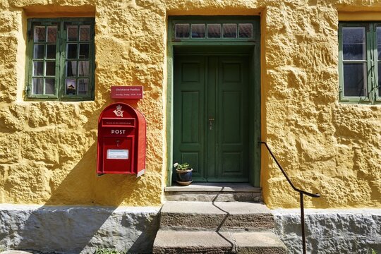 Post office, fa&ccedil;ade detail, red mailbox with post horn and crown, green wooden door, yellow wall, Christians&oslash;, Christians&ouml;, Ertholmene, Pea Islands, Bornholm, Baltic Sea, Denmark