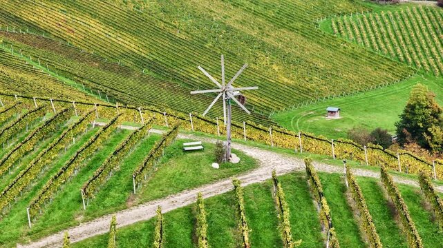 Aerial view of a traditional Klapotetz windmill standing among the rolling vineyard rows and autumn foliage in Gamlitz, Styria, Austria.