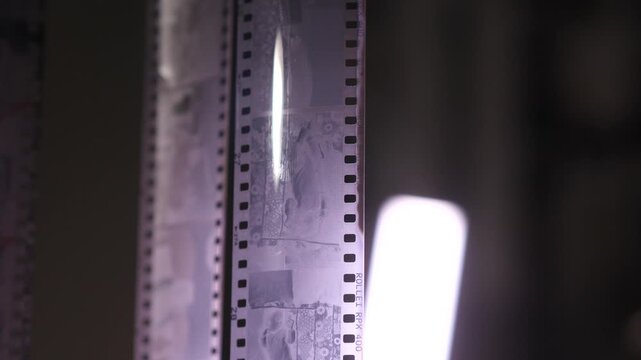 Film strip showing individual photographic frames on a developed negative, with a bright light illuminating the analog medium and its images in a darkroom environment