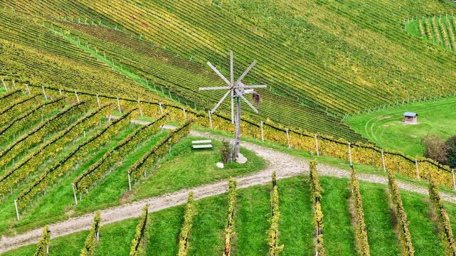 Aerial view of a traditional Klapotetz windmill standing among lush green vineyard rows on the rolling hills of Sudsteiermark in Gamlitz, Styria, Austria.