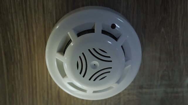 Smoke detector alarm system activation on wooden ceiling with warning red light flashing.