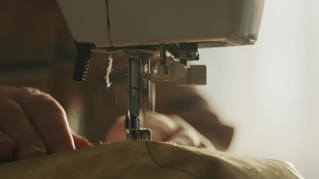 Close up of sewing machine needle stitching fabric in professional atelier or home workshop.