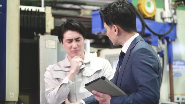 製造業の工場現場で作業着の技術者と営業が機械を見ながら見積もりや修理、メンテナンスの金額を悩む考えるのシーンの動画