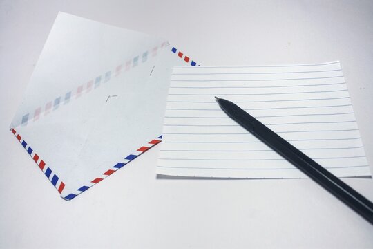 A black ballpoint pen resting on a blank lined paper next to an open airmail envelope on a white background
