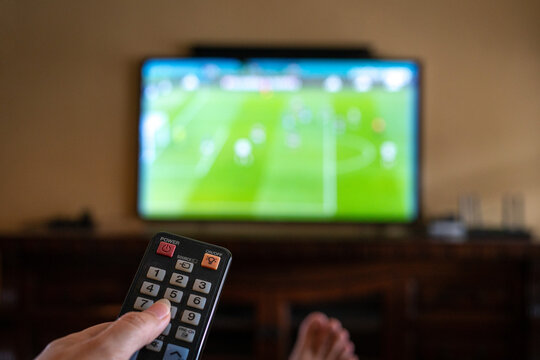 Watching football match at home. Remote control with tv screen at the background.