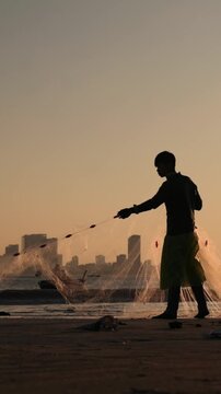 Vertical screen Casting Net During Sunrise. Sunrise Captures Fisherman As He Casts Net Over Water. Early Morning Fisherman In Da Nang Casting Net With Focused Hand Movement Over Shimmering