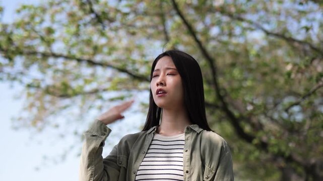 手で扇ぎながら木陰で涼む女性