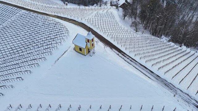 Aerial view of Dreisiebner Kapelle surrounded by snow-covered vineyard rows and a winding road in Gamlitz, Styria, Austria.