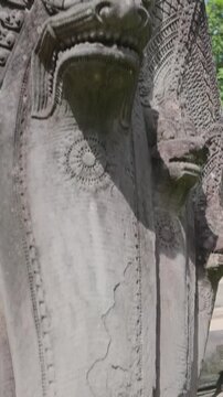A stone carving of a multi-headed Naga serpent guards the entrance to an ancient temple of Prasat Beng Mealea in Siem Reap, Cambodia. The intricate details showcase traditional Khmer artistry.