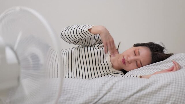 家の中でベッドに横たわって扇風機の風にあたる女性