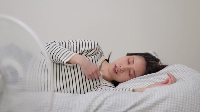 家の中でベッドに横たわって扇風機の風にあたる女性のズームイン