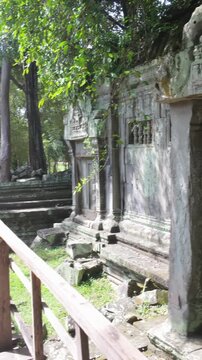 Ancient stone ruins overgrown with moss and vines, featuring intricate carvings and barred windows, in Prasat Beng Mealea, Siem Rep, Cambodia. The weathered facade evokes a sense of history and decay.
