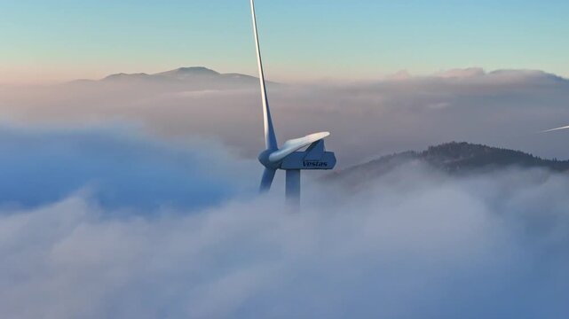 Aerial view of a wind turbine emerging from thick white clouds at Windpark Freilanderalm with mountains in the background Modriach, Styria, Austria.