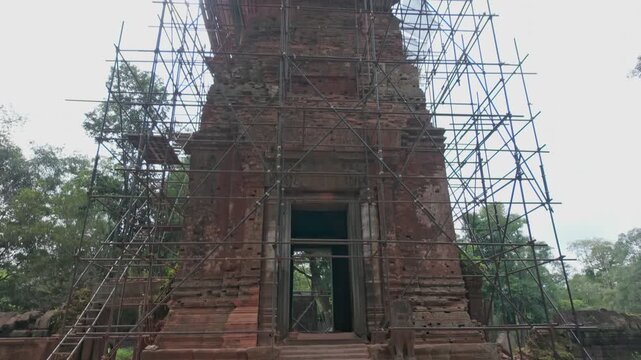 Ancient temple ruins in Kaoh Ker, Siem Reap, Cambodia. are undergoing restoration, with scaffolding surrounding the weathered brick structure. The site is being preserved for future generations.