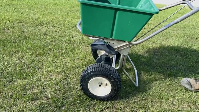 Close up of a green lawn fertilizer spreader on fresh grass during yard maintenance and landscaping work on a sunny summer day. Fertilizer Spreader On Grass. 
