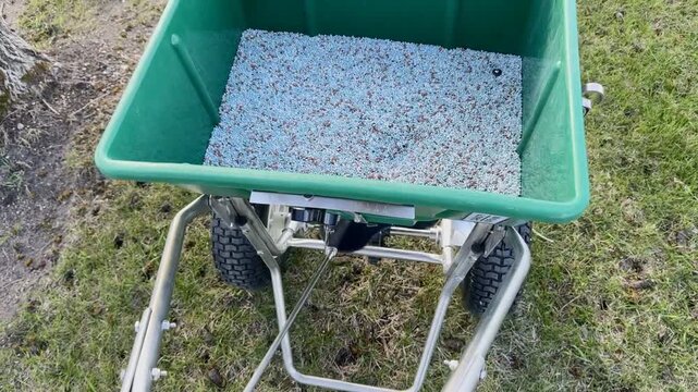 Close up of a green lawn fertilizer spreader on fresh grass during yard maintenance and landscaping work on a sunny summer day. Fertilizer Spreader On Grass. 